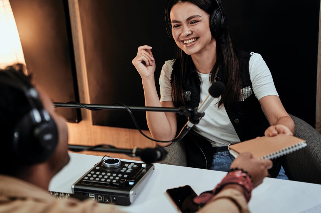 Portait of happy female radio host laughing while talking with male guest, presenter and giving