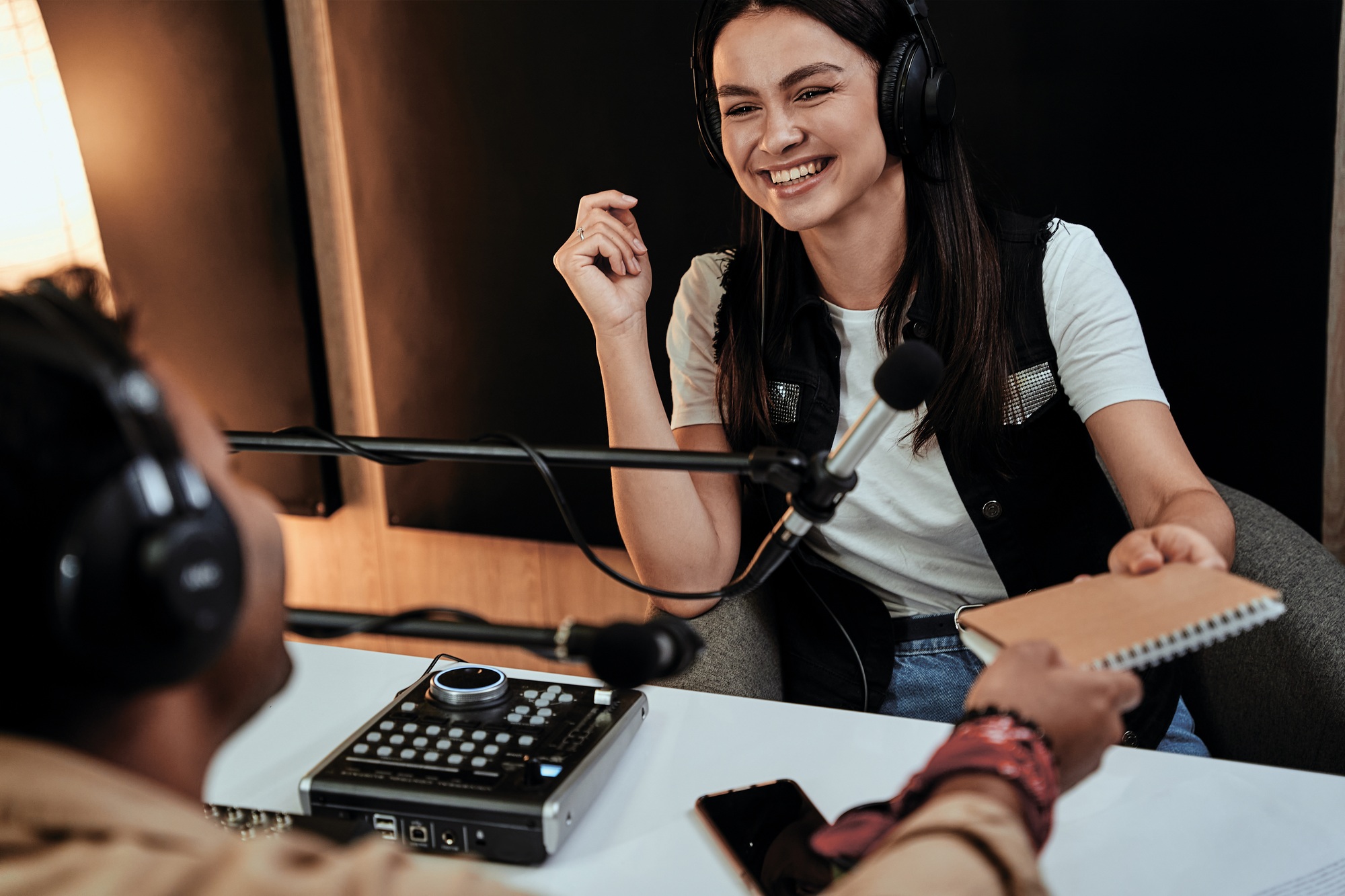 Portait of happy female radio host laughing while talking with male guest, presenter and giving
